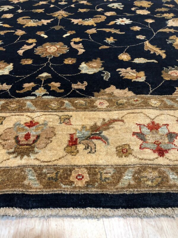 Navy blue high-pile rug with tan floral motifs and a detailed beige border on a light wood floor.