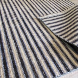 A rolled-back rug with thick alternating beige and dark brown stripes rests on light wood flooring.