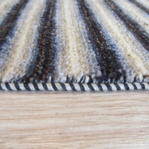 Close-up shows shaggy cream, brown, and blue striped rug pile and binding on light wood floor.