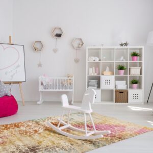 Colorful abstract rug with pink and gold tones anchors a white rocking horse in a bright nursery.