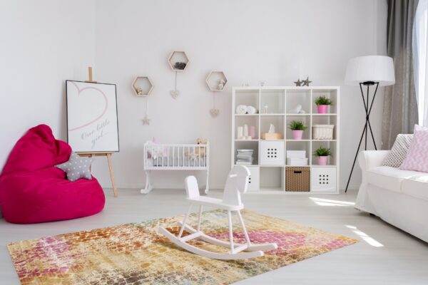 Colorful abstract rug with pink and gold tones anchors a white rocking horse in a bright nursery.