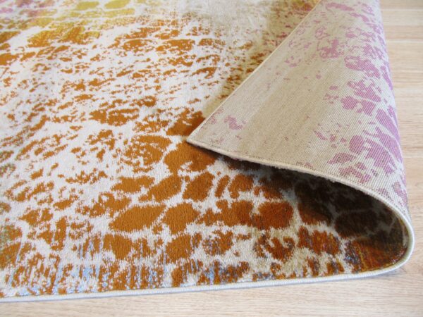 A rust and cream abstract low-pile rug lies on wood flooring with the patterned backing revealed.