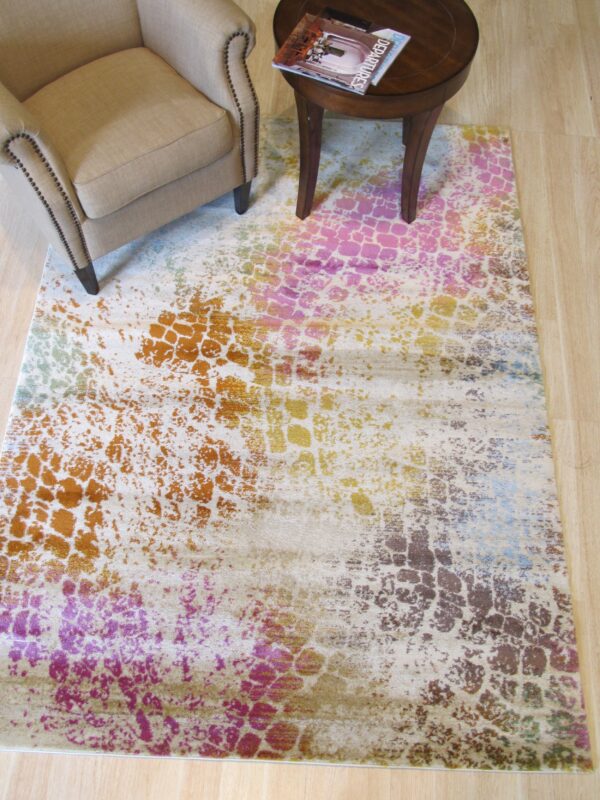 Abstract rug in beige, pink, orange, and brown sits beneath a neutral armchair and dark wood side table.
