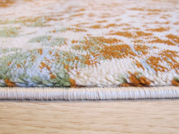 A textured pile rug with off-white, green, and orange abstract shapes rests on light wood.