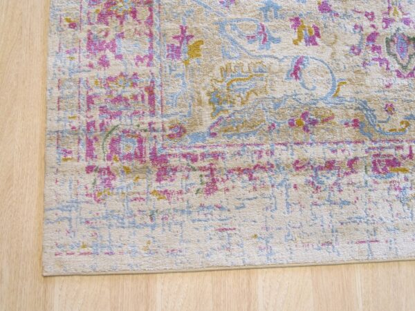 Distressed beige rug featuring traditional magenta, blue, and yellow patterns on light wood planks.
