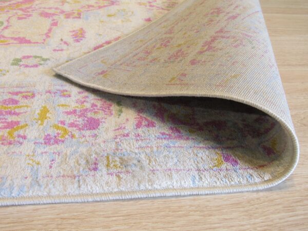 Low pile rug in cream, pink, and yellow, showing the woven backing on light wood floors.