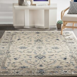 Cream rug with blue traditional floral patterns rests on dark flooring near a white table and wood chair.