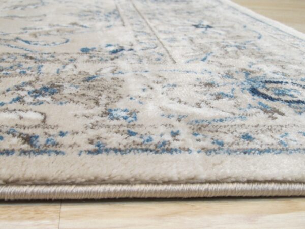 Cream rug with visible medium pile features a distressed pattern in blue and taupe on light wood.