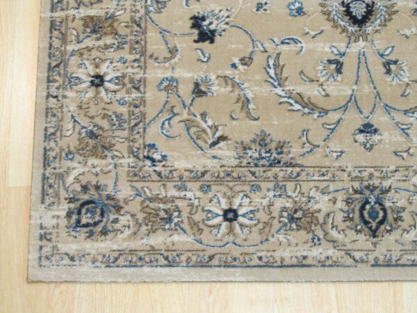 Traditional beige area rug with ornate blue, brown, and cream border rests on light planked wood.