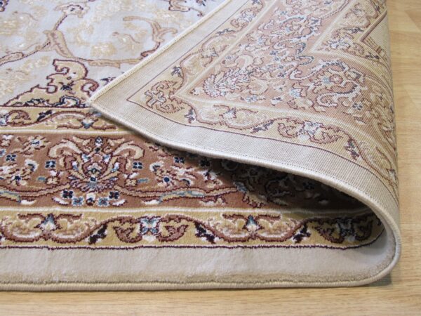 Beige and brown traditional rug with floral motifs folded on light wood flooring, showing the woven backing.