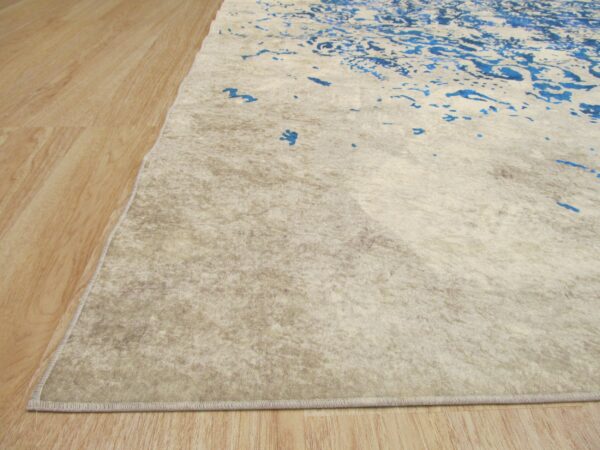 Low-pile rug in textured beige and blue abstract patterns rests on light wood-look flooring.