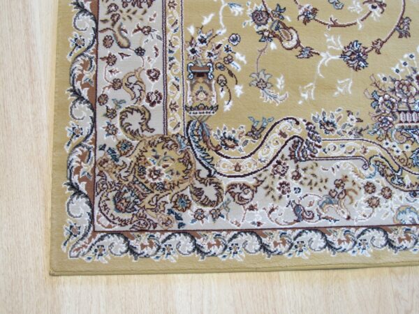 Ornate yellow rug corner showing floral patterns in brown, cream, and blue over light wood planks.