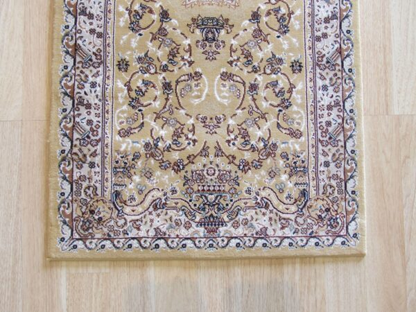Low-pile traditional tan rug with brown, cream, and blue accents, displayed on light wood plank flooring.