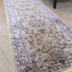 Traditional runner rug in tan, cream, and rust colors lies on light wood flooring next to a chair.