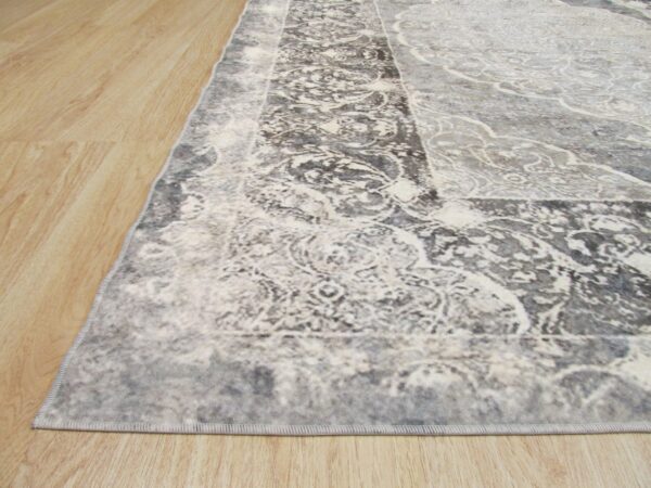 Close-up of a low-pile gray and white distressed traditional rug on light wood plank flooring.