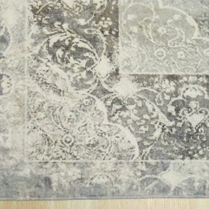 Distressed traditional rug featuring grey and cream ornate patterns rests on light natural wood planks.