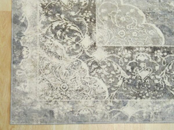 Distressed grey and cream rug featuring an ornate traditional pattern border rests on light wood flooring.