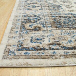 Low-pile cream rug with distressed blue and taupe traditional patterning sits on light wood flooring.