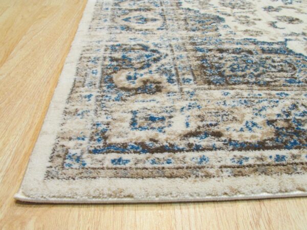 Low-pile cream rug with distressed blue and taupe traditional patterning sits on light wood flooring.