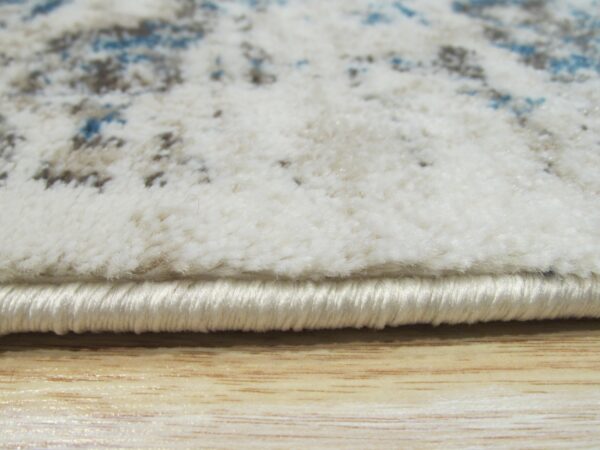 Detail of a fluffy white rug with abstract blue and taupe patterns over light wooden flooring.