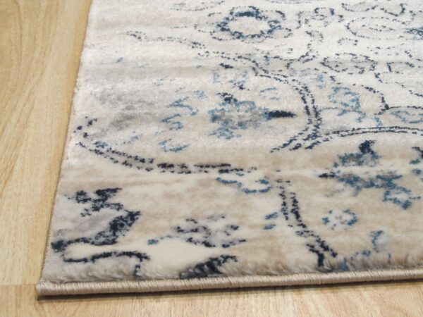 Close-up of a cream rug with navy and light blue distressed patterns resting on light wood flooring.