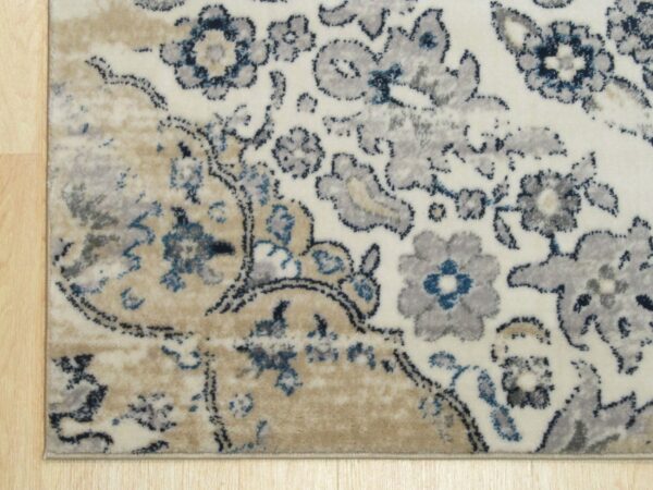 Cream rug with distressed gray, navy, and beige floral patterns rests on light wood flooring.