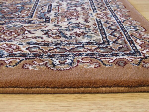 Low-pile rug with ornate pattern in cream, blue, and brown, featuring a wide solid tan border on wood flooring.