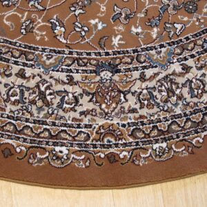 The curved edge of a brown, traditional rug with beige and blue accents lies on wood flooring.