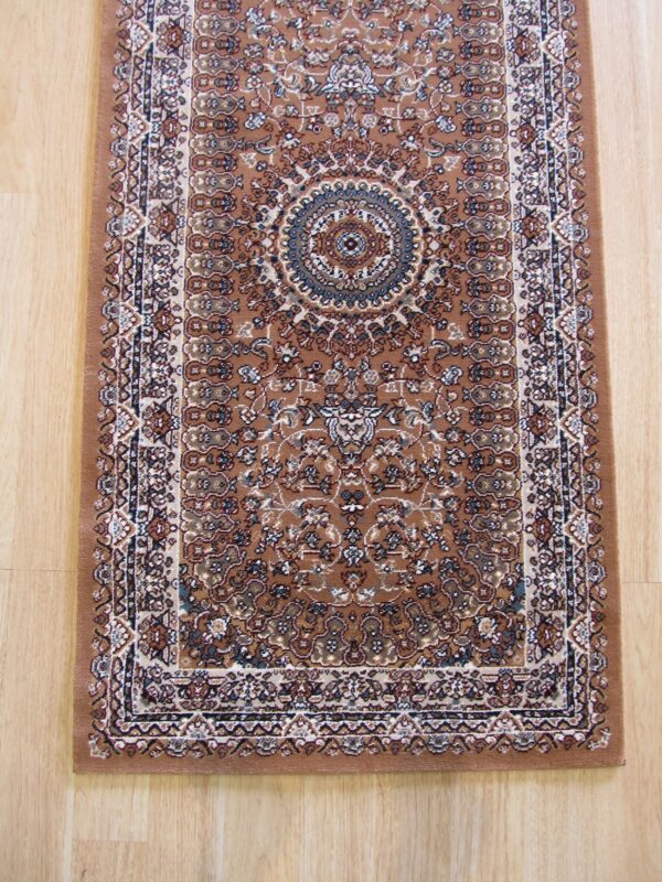 A narrow brown runner rug featuring a detailed traditional medallion pattern in cream and blue rests on light wood flooring.