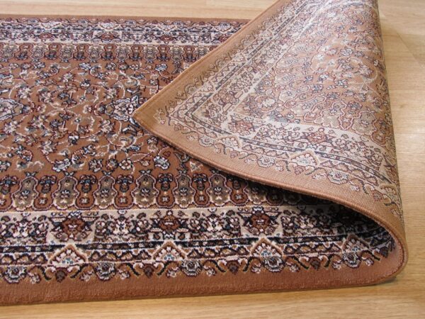 Close-up of a brown floral patterned rug curled back, revealing the light woven backing on a wood floor.
