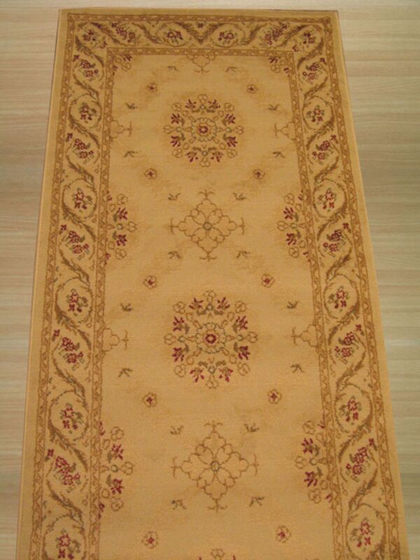 Tan runner rug featuring a detailed floral border and central burgundy accents on light wood plank flooring.