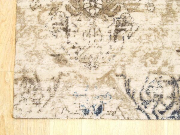 Distressed beige rug featuring faded brown and blue patterns rests on light blonde hardwood floor.
