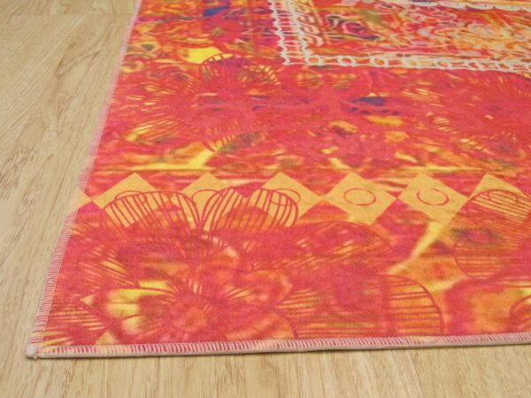 Vibrant low-pile rug displaying pink, red, and yellow botanical and geometric patterns on a wood floor.