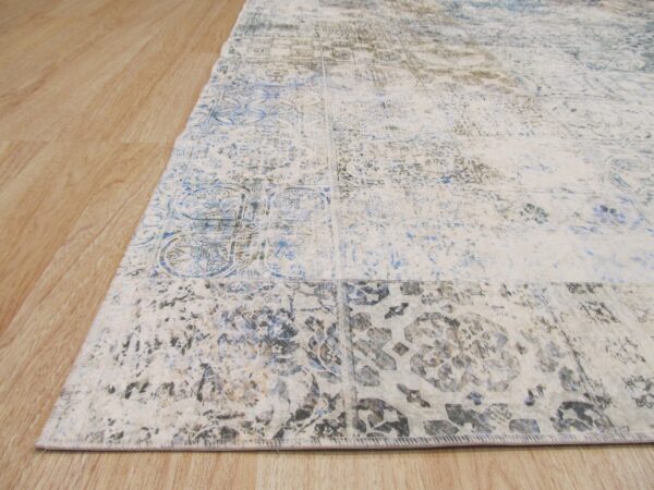 Low-pile rug in cream, faded blue, and gray distressed medallion patterns rests on wood flooring.
