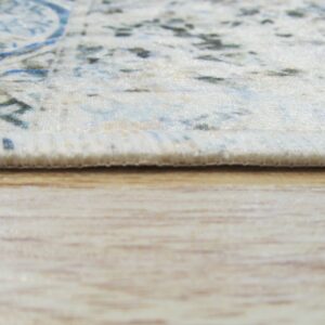 Close-up shows the thin, bound edge of a cream and blue rug against light wood flooring.