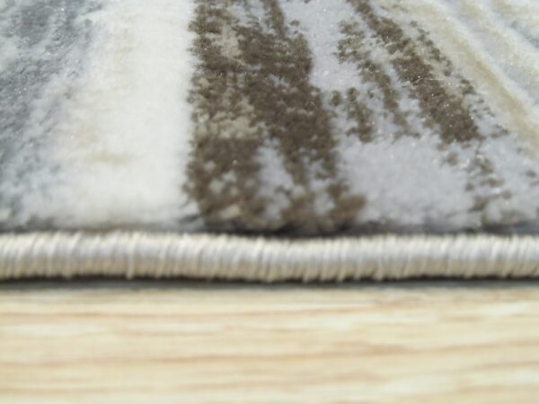 The rug's edge and high pile feature streaked gray, white, and taupe abstract patterns resting on wood flooring.