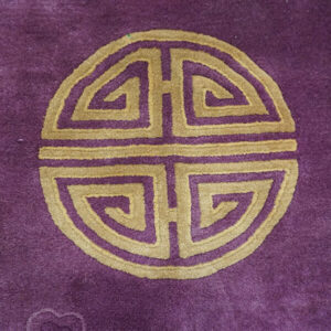 Deep purple rug with a circular gold geometric pattern, showing a soft, plush pile texture.
