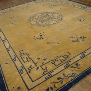 Low-pile gold rug with dark blue floral and geometric designs rests on distressed hardwood flooring.