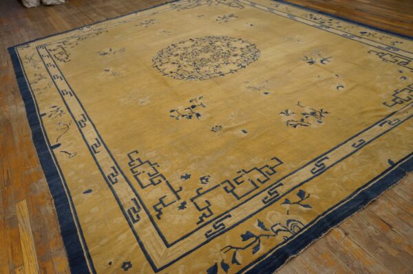 Low-pile gold rug with dark blue floral and geometric designs rests on distressed hardwood flooring.