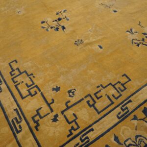 Mustard yellow area rug with navy blue Greek key border and subtle scattered floral designs.