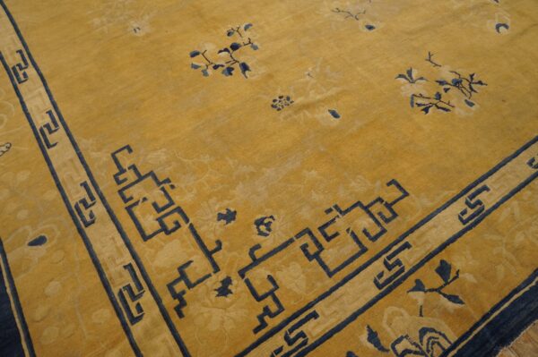 Mustard yellow area rug with navy blue greek key border and subtle scattered floral designs.