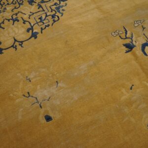 A textured golden yellow rug displays faded navy blue scrolling and floral designs.