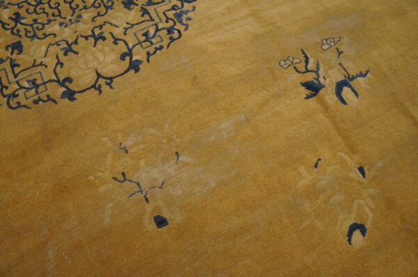 A textured golden yellow rug displays faded navy blue scrolling and floral designs.