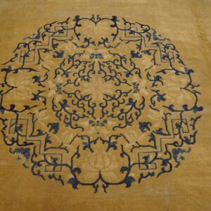 Gold rug featuring a dense circular medallion pattern of dark blue floral and angular motifs.