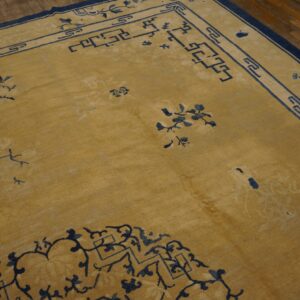 Gold low-pile rug with navy floral and geometric borders rests on a dark plank wood floor.