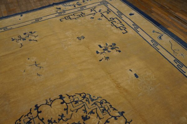 Gold low-pile rug with navy floral and geometric borders rests on a dark plank wood floor.