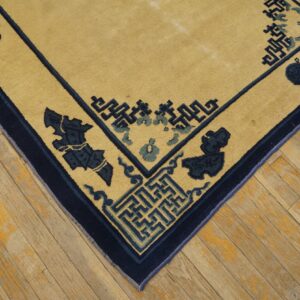 Golden rug corner featuring geometric fretwork and navy floral motifs rests on worn light wood planks.
