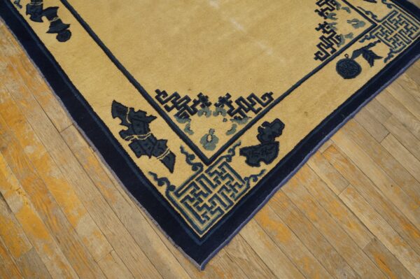 Golden rug corner featuring geometric fretwork and navy floral motifs rests on worn light wood planks.