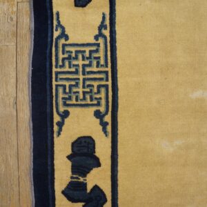 Detail of a yellow rug with a navy geometric border on light wood flooring.