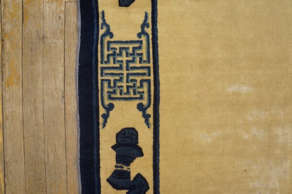 Detail of a yellow rug with a navy geometric border on light wood flooring.